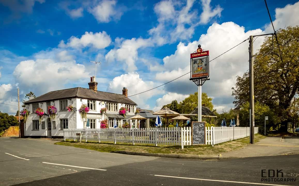 The Chandos Arms pub on a sunny day, a white-rendered country inn with hanging flower baskets, a traditional pub sign and a fenced beer garden.