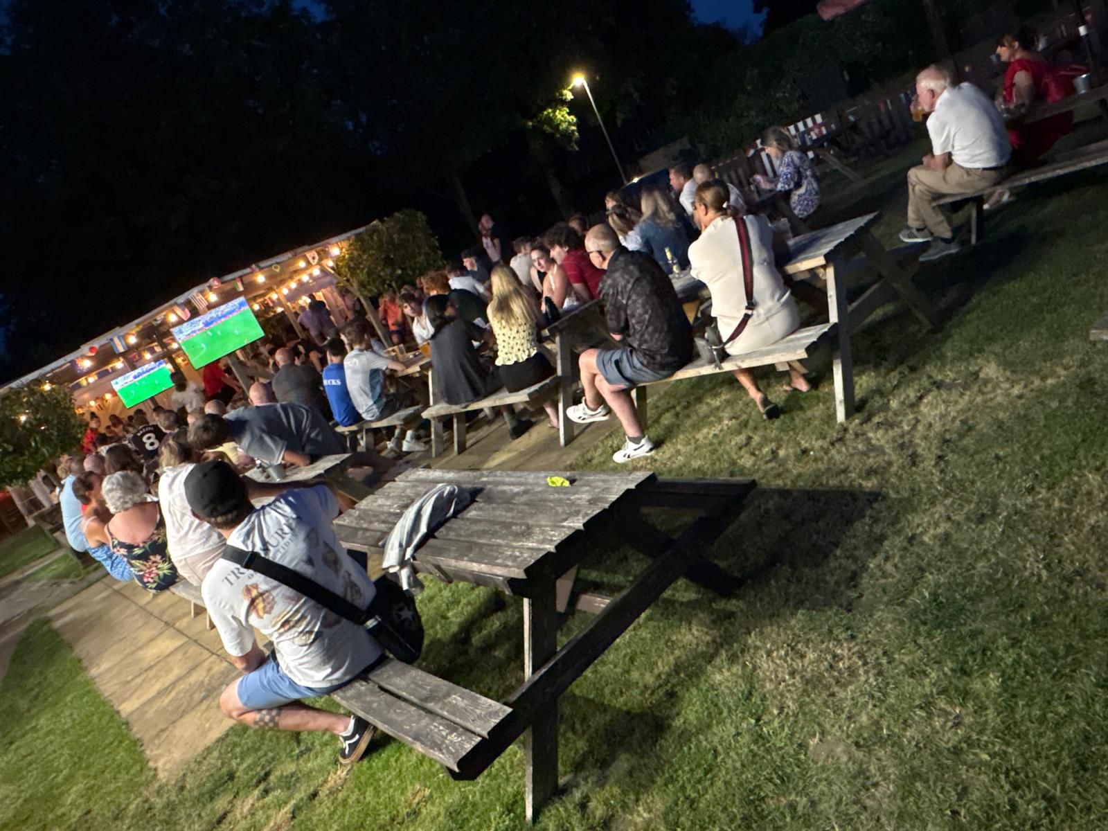 A crowd gathered in the garden at The Chandos Arms watching live football on a big screen on a summer evening.