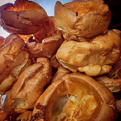 A close-up of a pile of large, deep golden Yorkshire puddings fresh from the oven